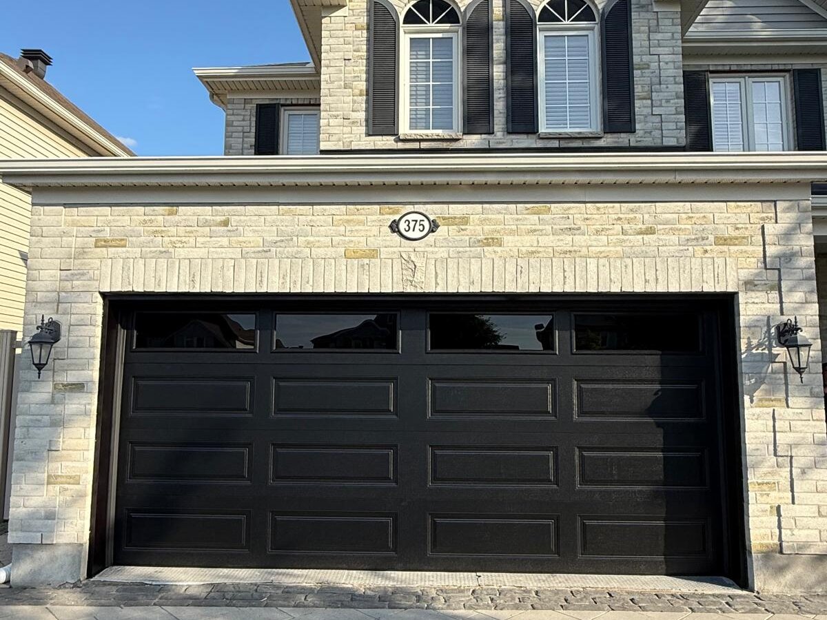 Black modern flush-panel double garage door on a stone-front GTA home