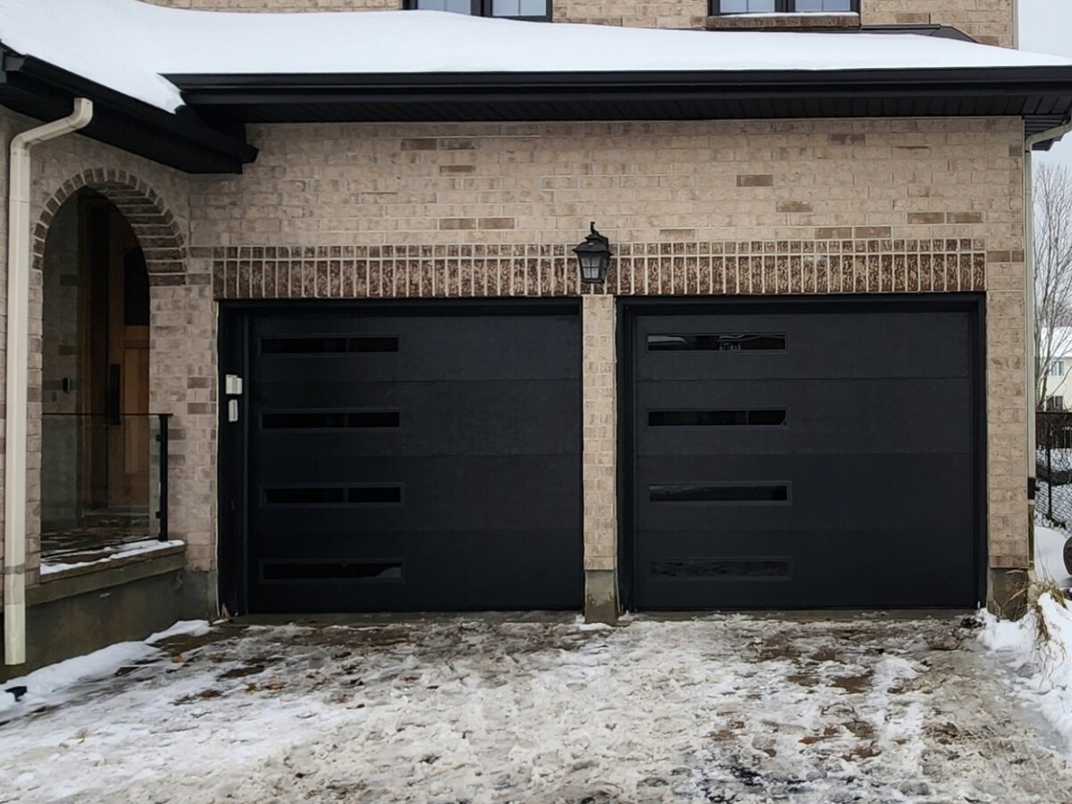 Black contemporary garage door with vertical glass accents beside an arched brick entry