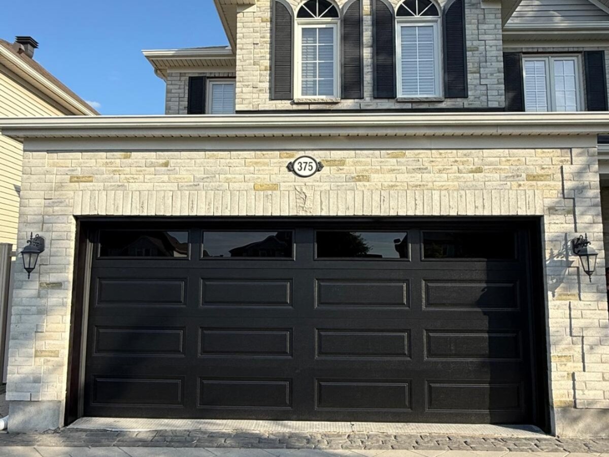 Black raised-panel double garage door on a stone-front two-storey home