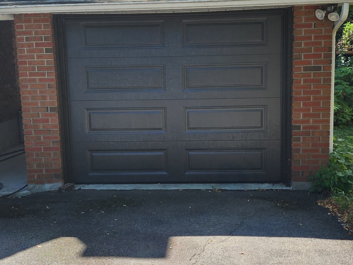 Charcoal grey raised-panel single garage door on a brick home