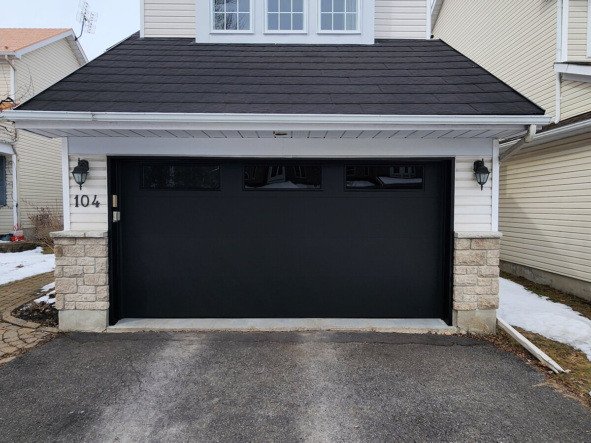 Black raised-panel single garage door on a home with a dark roof