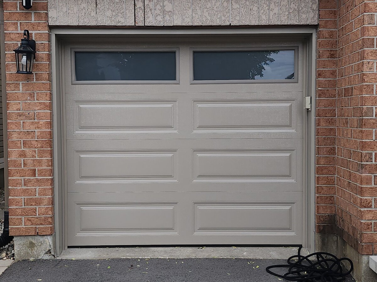 Tan raised-panel single garage door with windows on a brick home