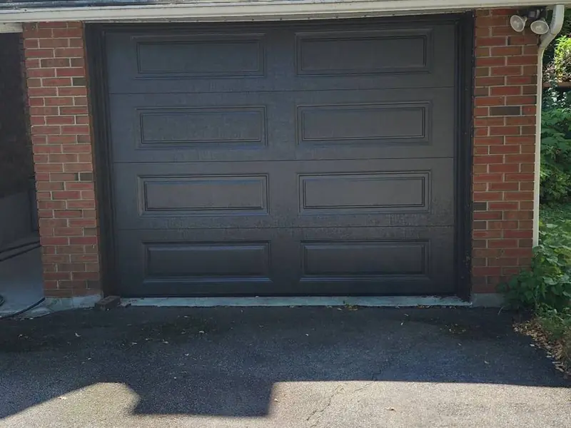 Charcoal grey raised-panel single garage door on a brick home