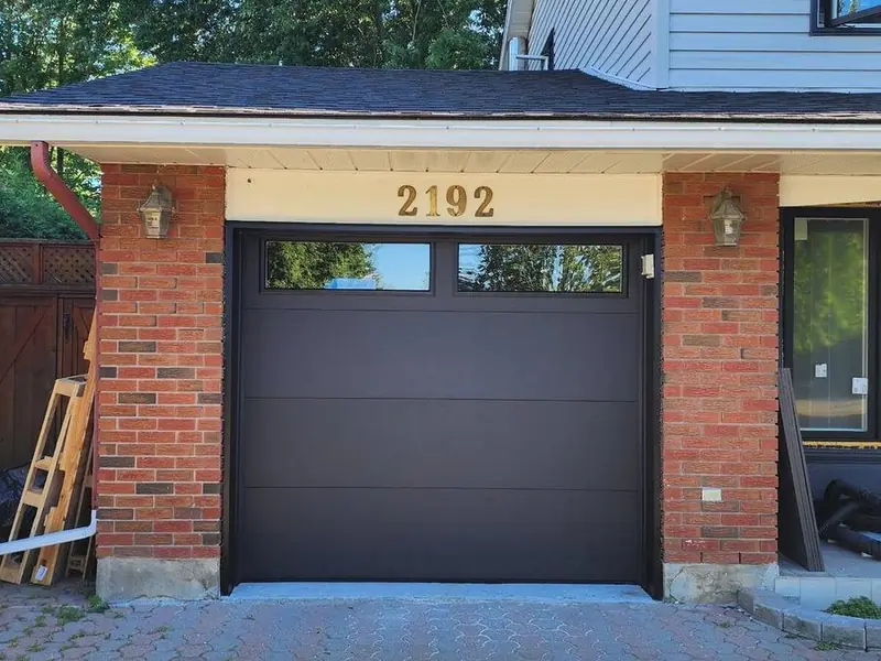 Dark brown flush-panel single garage door on a two-tone brick home