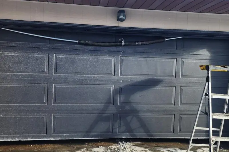 DPS Garage Doors repairing the torsion spring on a dark double garage door with a ladder set up in the GTA
